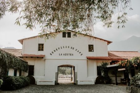 Charming historic building of Beneficio de Cafe La Azotea surrounded by lush greenery and cobblestones.